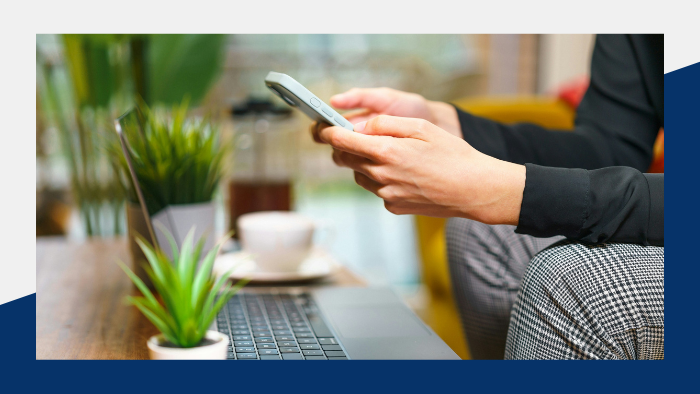 Person holding a smartphone in front of an open laptop