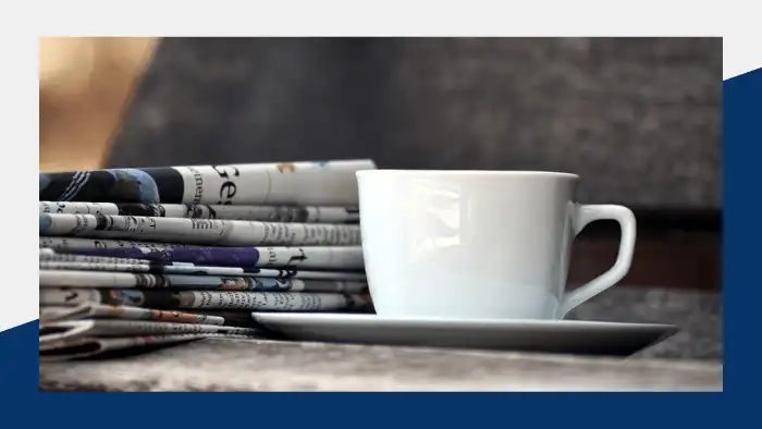 Coffee cup next to a stack of newspapers