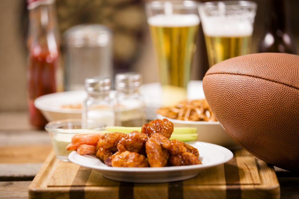 A football on a table with wings, beer and pretzels