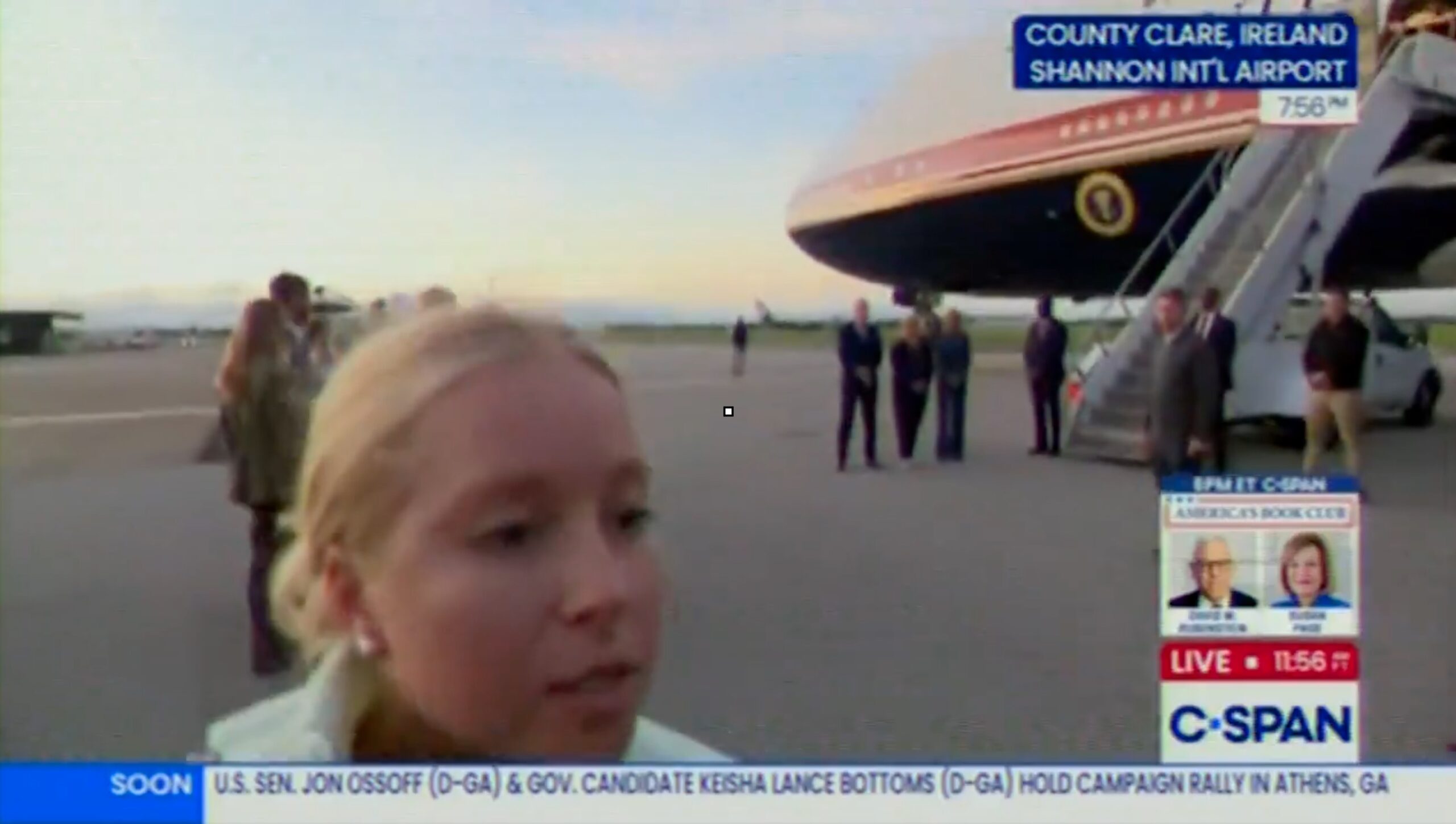 screenshot showing blonde woman close to camera on a tarmac pushing back reporters